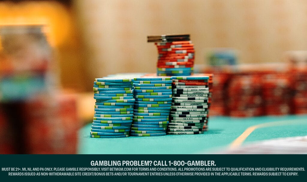Stacks of colorful poker chips arranged on a green casino table, with various denominations in blue, red, black, and white. The background is blurred.
