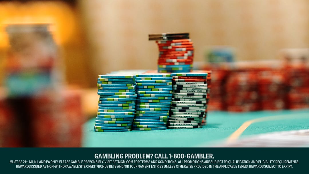 Stacks of colorful poker chips arranged on a green casino table, with various denominations in blue, red, black, and white. The background is blurred.