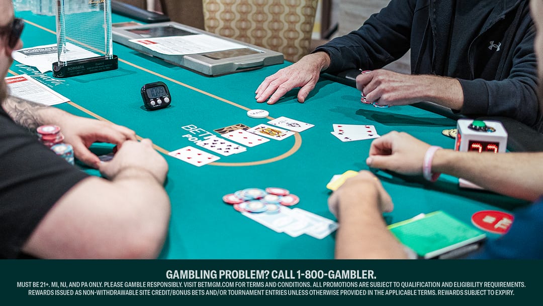 Three poker players sitting at a poker table. There are five community cards on the table and one poker hand face up.
