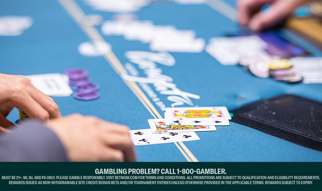 Looking down at a poker table. There are four cards loosely lined up in front of a player. In the background is an out-of-focus stack of chips and another player’s hand.