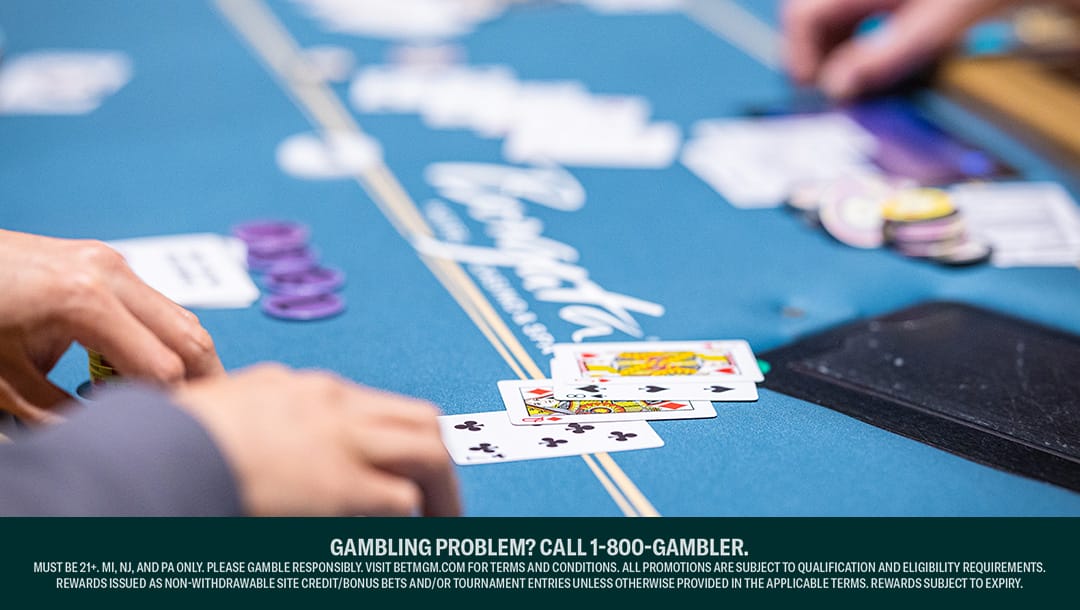 Looking down at a poker table. There are four cards loosely lined up in front of a player. In the background is an out-of-focus stack of chips and another player’s hand.