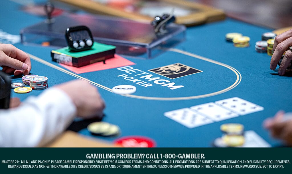 Close-up of players at a BetMGM Poker table, with poker chips and playing cards on the felt surface branded with the BetMGM logo.