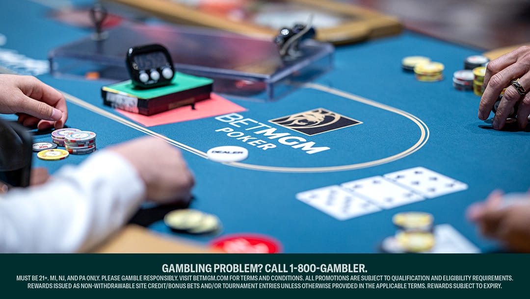 Close-up of players at a BetMGM Poker table, with poker chips and playing cards on the felt surface branded with the BetMGM logo.