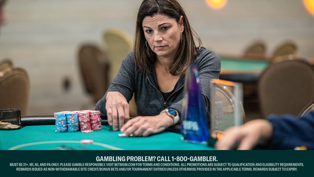 A woman places her hand next to stacks of blue and red poker chips during a poker game.