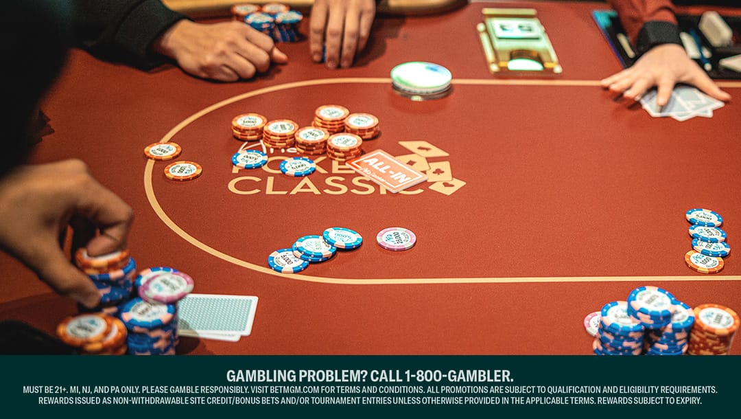 A view of a red poker table at the Aria Poker Classic. There are face-down cards and stacks of poker chips around the table, with players deciding their bets.