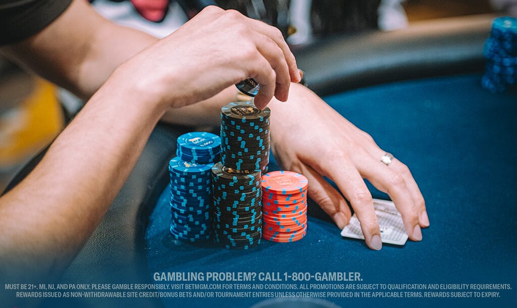 Close-up of a player stacking casino chips at a table while holding playing cards.