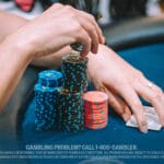 Close-up of a player stacking casino chips at a table while holding playing cards.